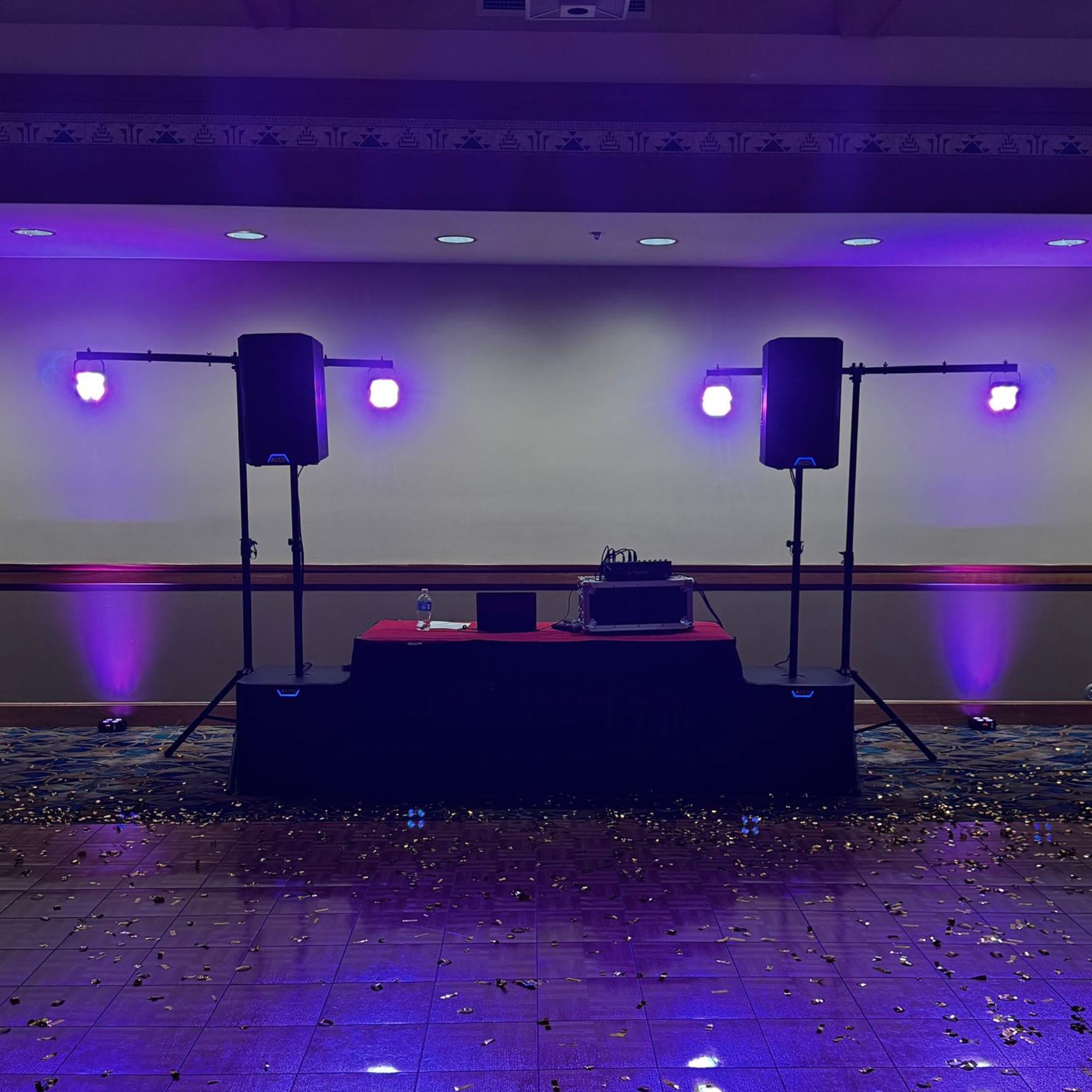 Empty event stage with two black speakers and purple lights reflecting on a confetti-covered floor