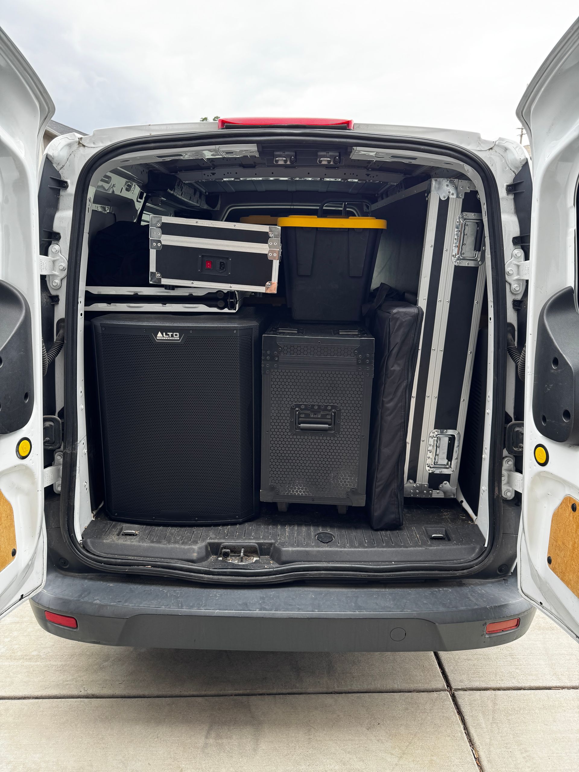 Open van cargo van with stacked black speaker cases and equipment inside.
