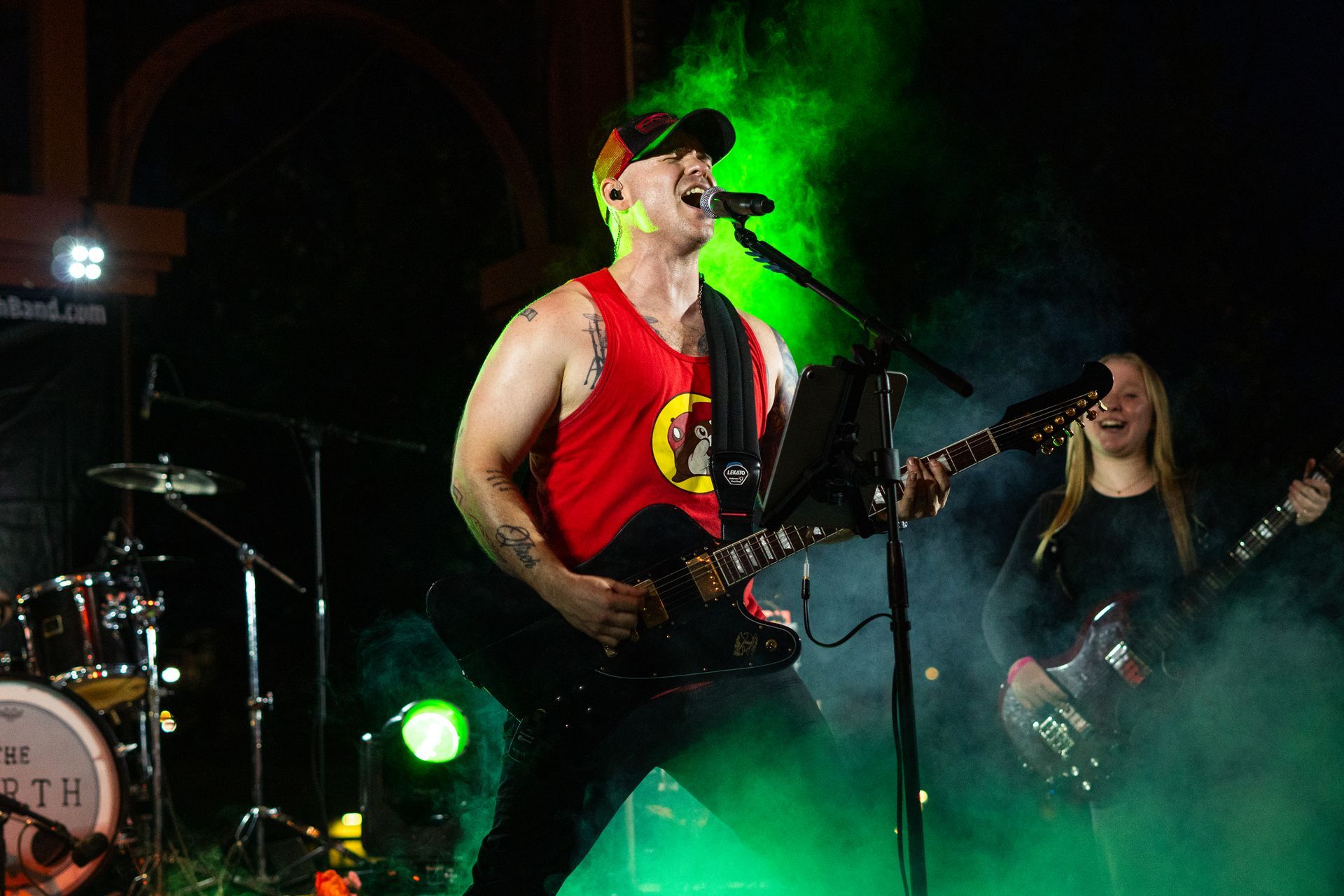 Singer playing guitar on a smoky stage under green lights, with a bandmate in the background
