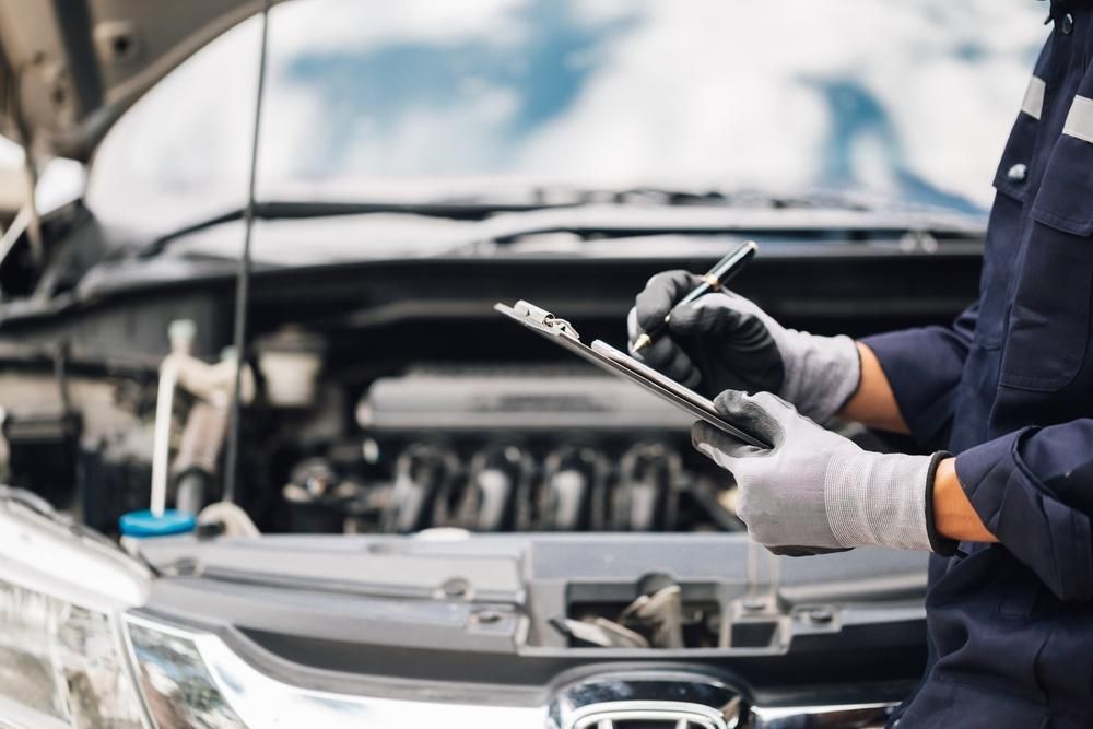 A Mechanic Is Writing On A Clipboard In Front Of A Car — SG Mobile Mechanic In Newcastle, NSW