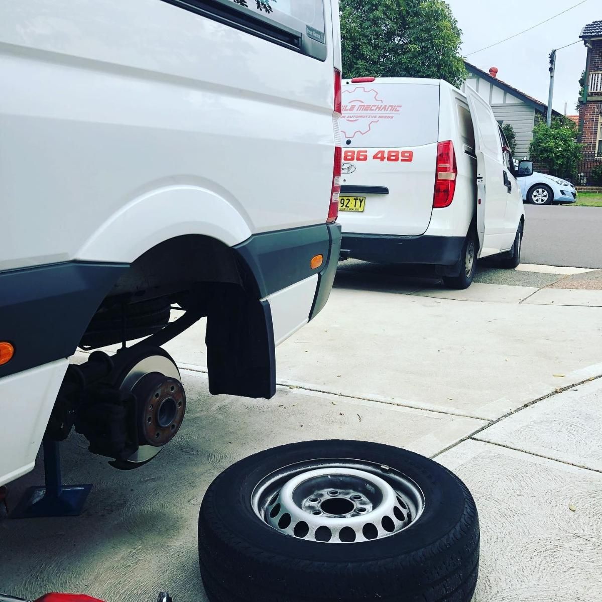 Two White Vans Are Parked In A Driveway With A Tire On The Ground — SG Mobile Mechanic In Newcastle, NSW