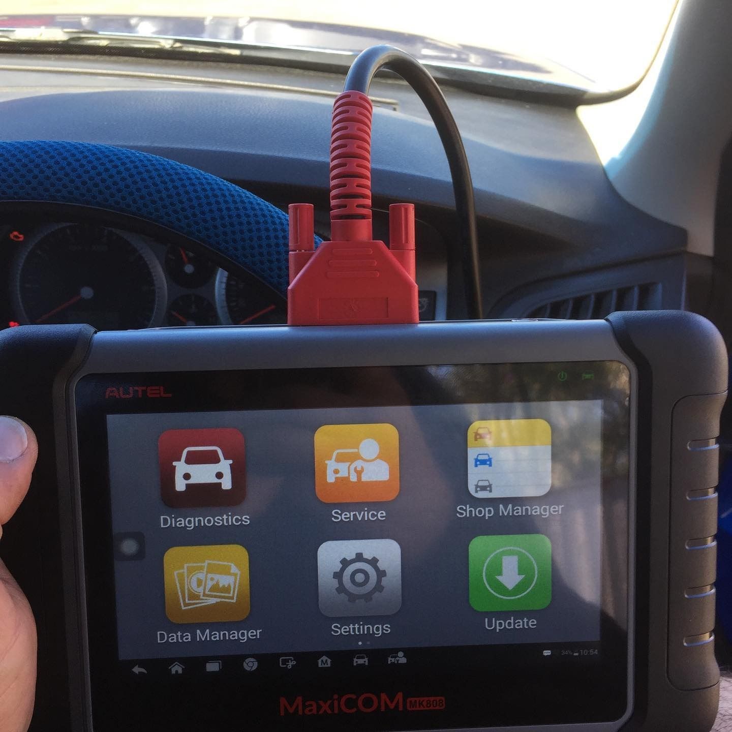 A Hand Is Holding A Maxicom Device In Front Of A Car — SG Mobile Mechanic In Newcastle, NSW