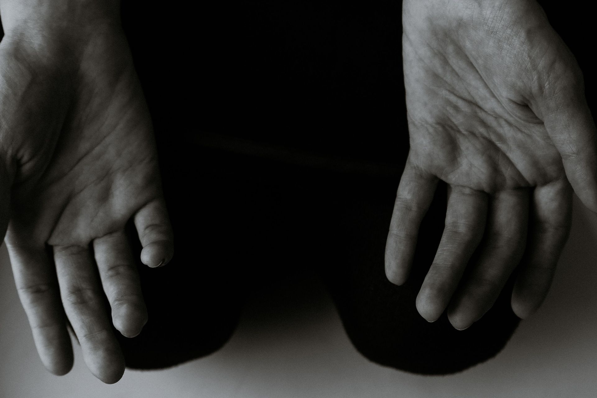 Two open hands resting on dark pants against a black background