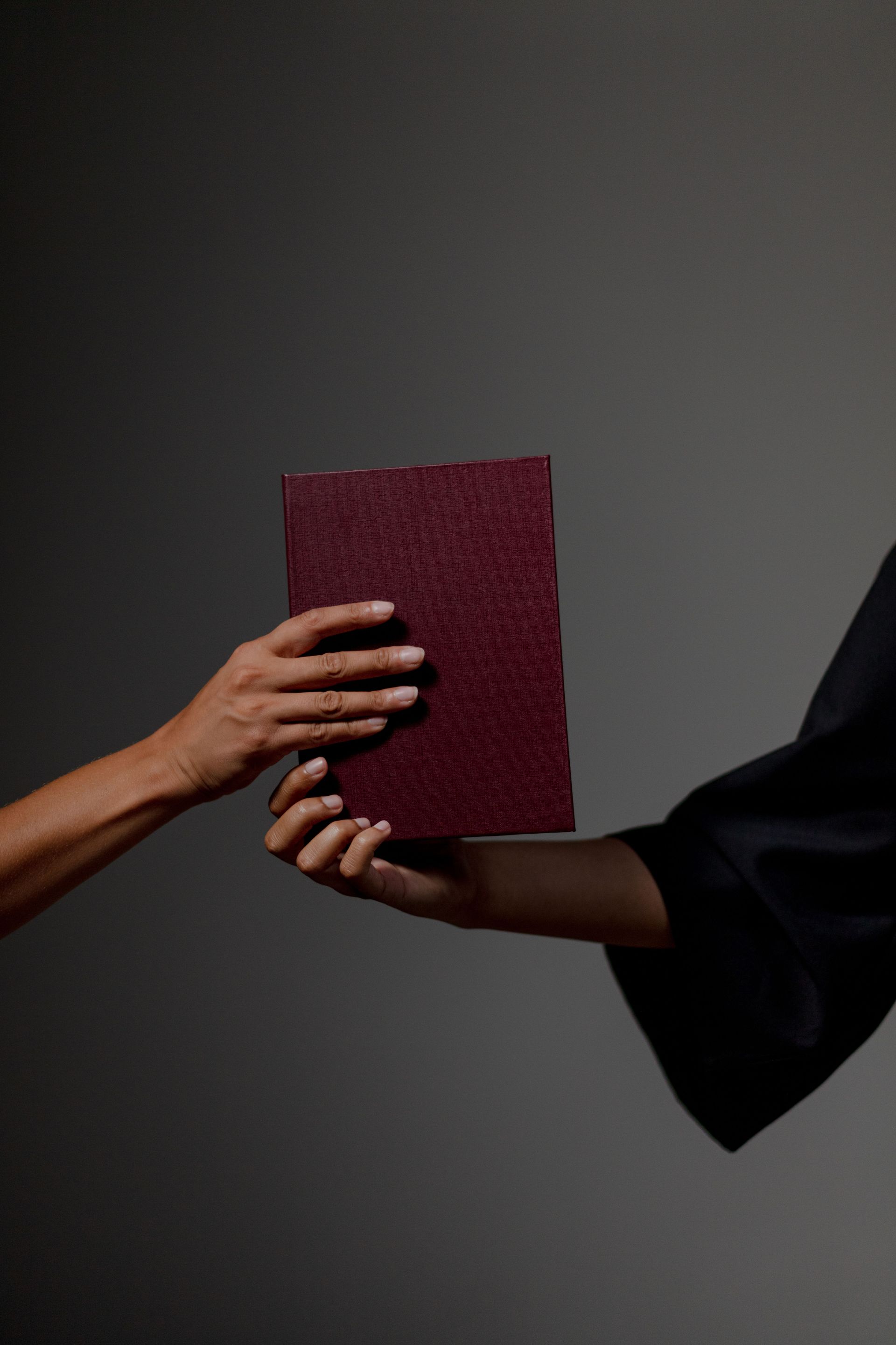 Two hands exchanging a red book against a dark background