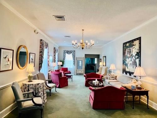 Elegant living room with red chairs, pale walls, chandeliers, and framed art
