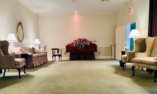 Elegant funeral parlor with beige seating and a flower-covered casket at the back center.