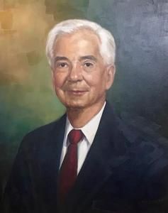 Studio portrait of a smiling man in a dark suit, white shirt, and red tie against a muted background