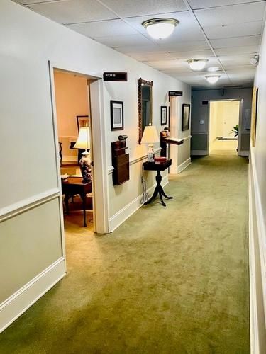 Office hallway with green carpet, white walls, open doorways, and wall-mounted lamps
