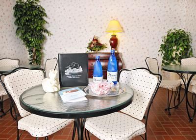 Cafe table with floral chairs, a lamp, blue vase, gift bag, and small decorative plants.