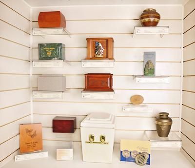White display shelves with assorted small boxes, jars, and decorative objects in a shop or gallery.