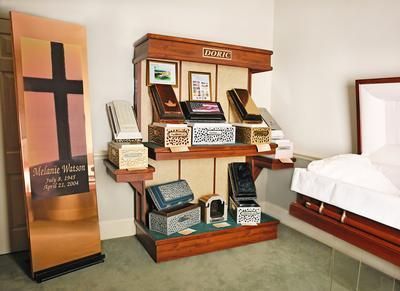 Coffin display in a funeral home showroom beside a white casket and sample memorial plaques.