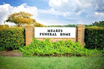 Meares Funeral Home sign on a brick-and-hedge entrance with green landscaping and cloudy sky