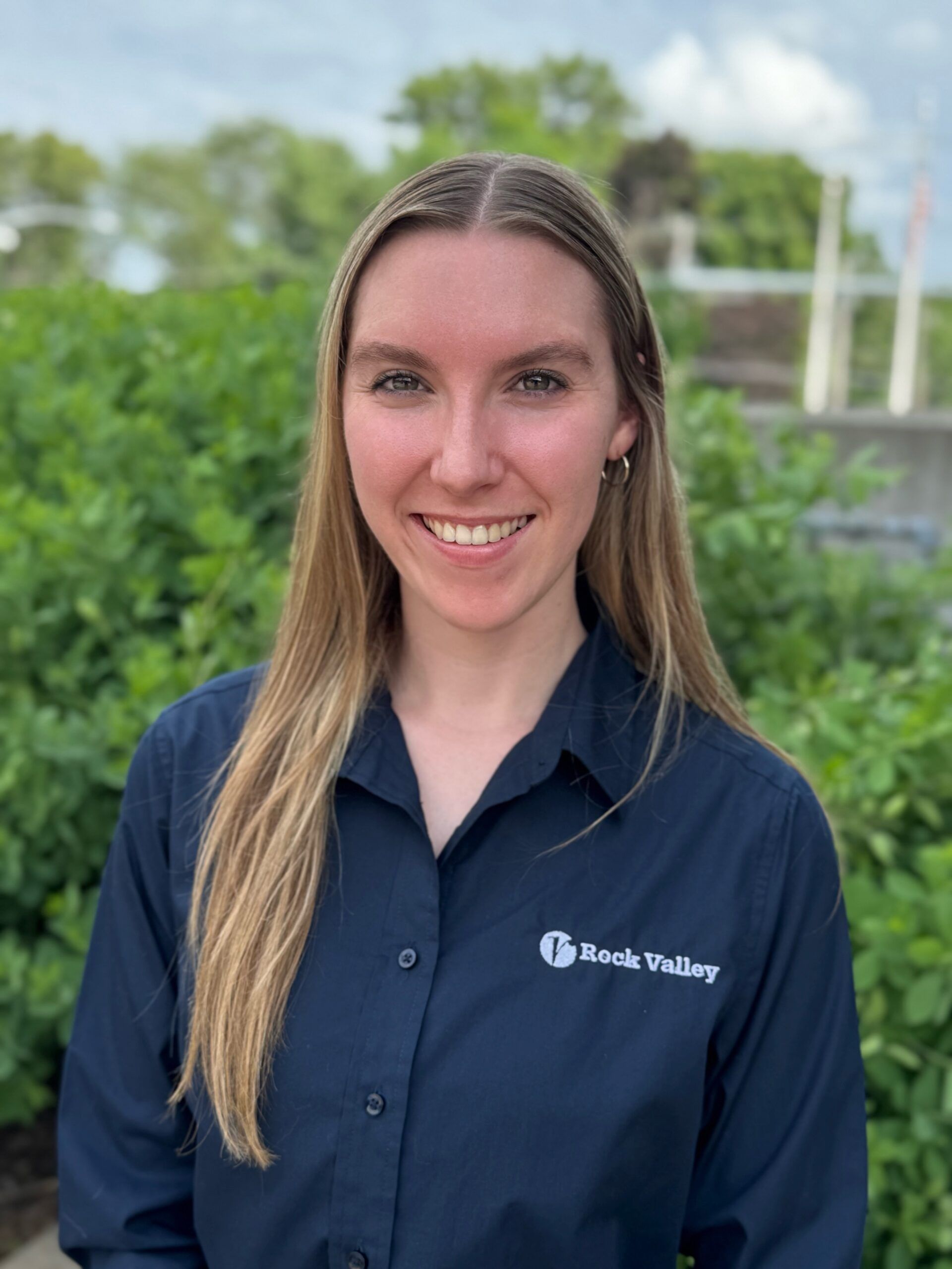 Woman in navy shirt smiling outdoors with greenery in the background