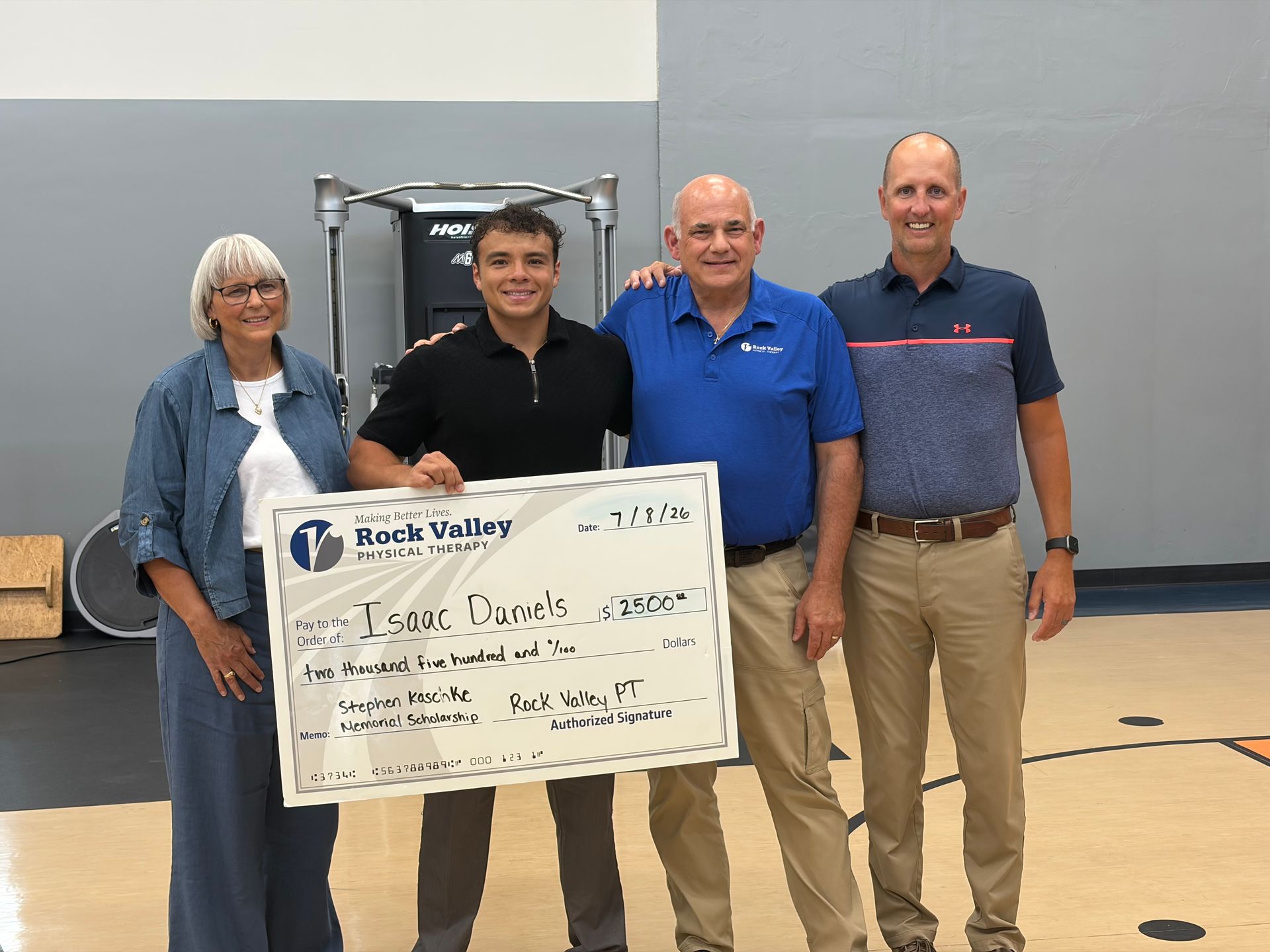 Four people stand in a gym holding an oversized check for Kord Valley.