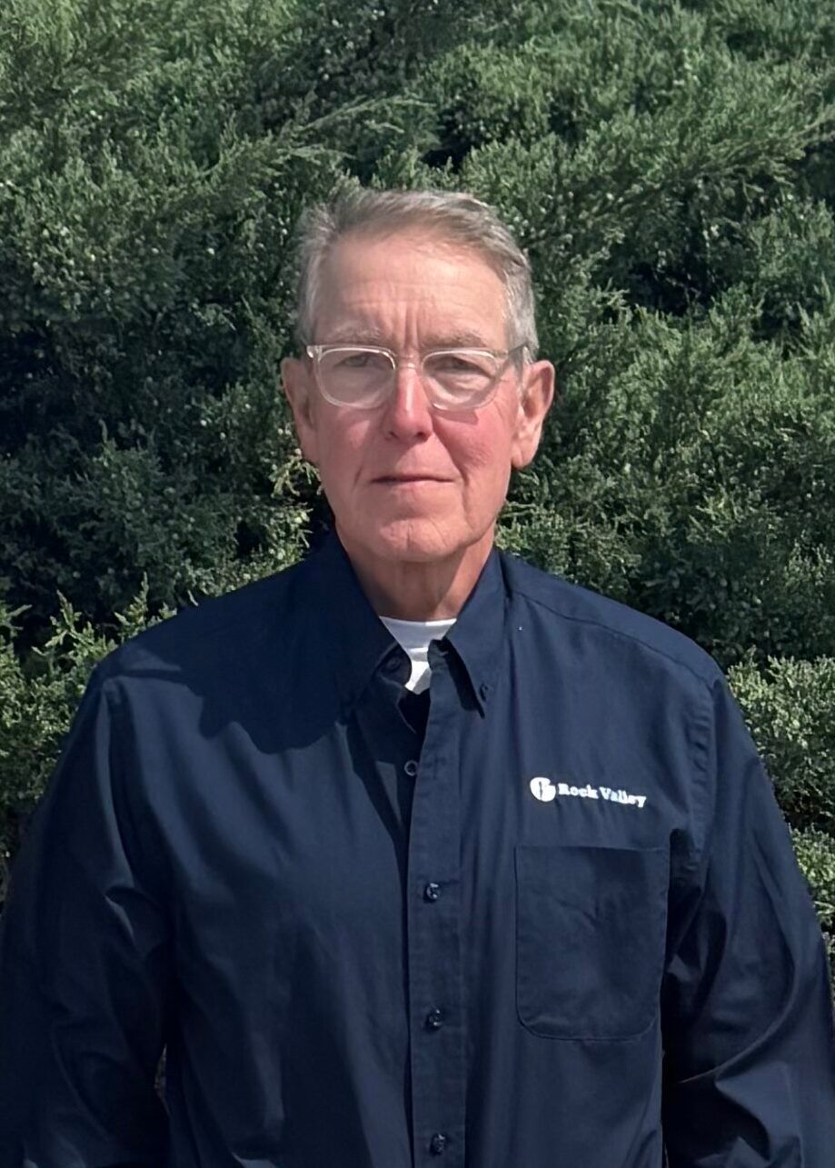 Man standing outdoors in a dark jacket with a green leafy background