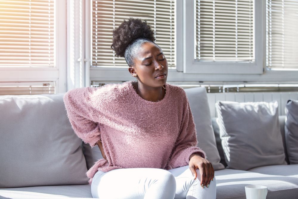 Person in a pink sweater sitting on a couch, leaning back and looking to the side in a bright living room.