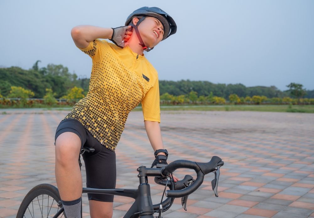 Cyclist in a yellow jersey posing with a bike on a paved path outdoors under a cloudy sky