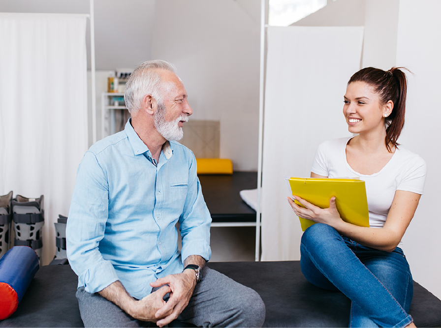 Older man and young woman talking on a couch, smiling, with a yellow tablet in a bright living room