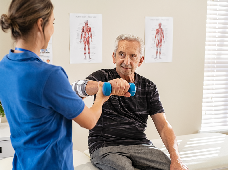 Therapist assists a man with weight lifting; he sits on a medical table, holding a dumbbell.