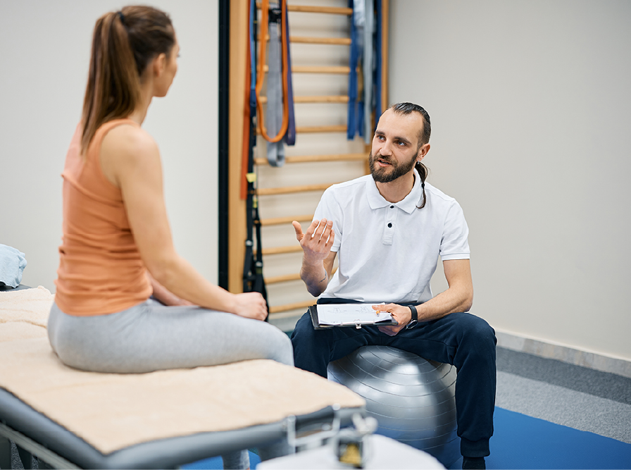 Physical therapist consulting with a patient seated on a treatment table.