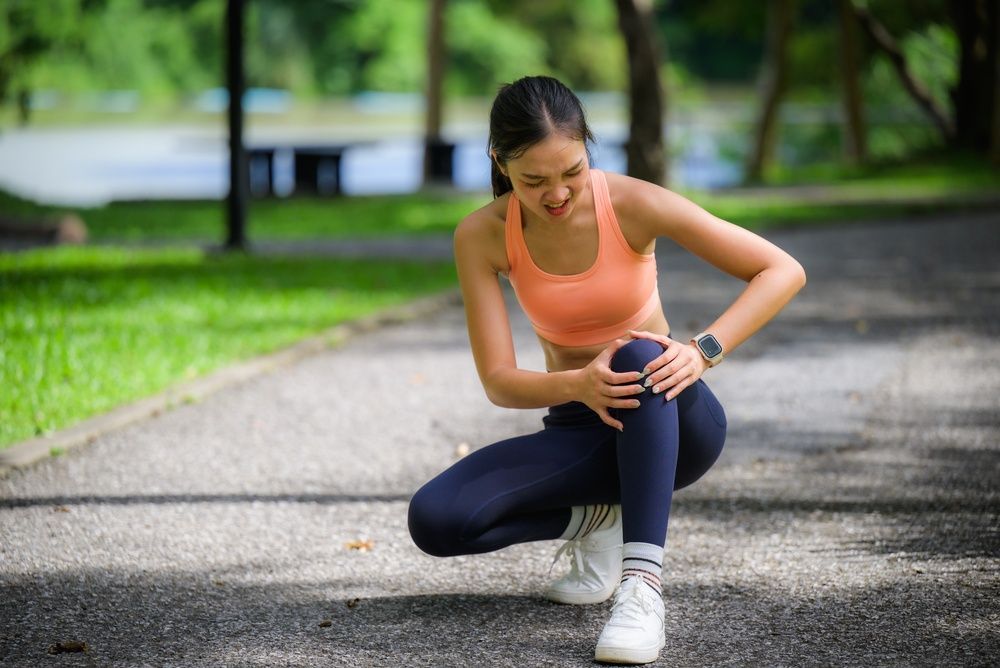 Runner crouching on a park path, checking her knee after a workout.