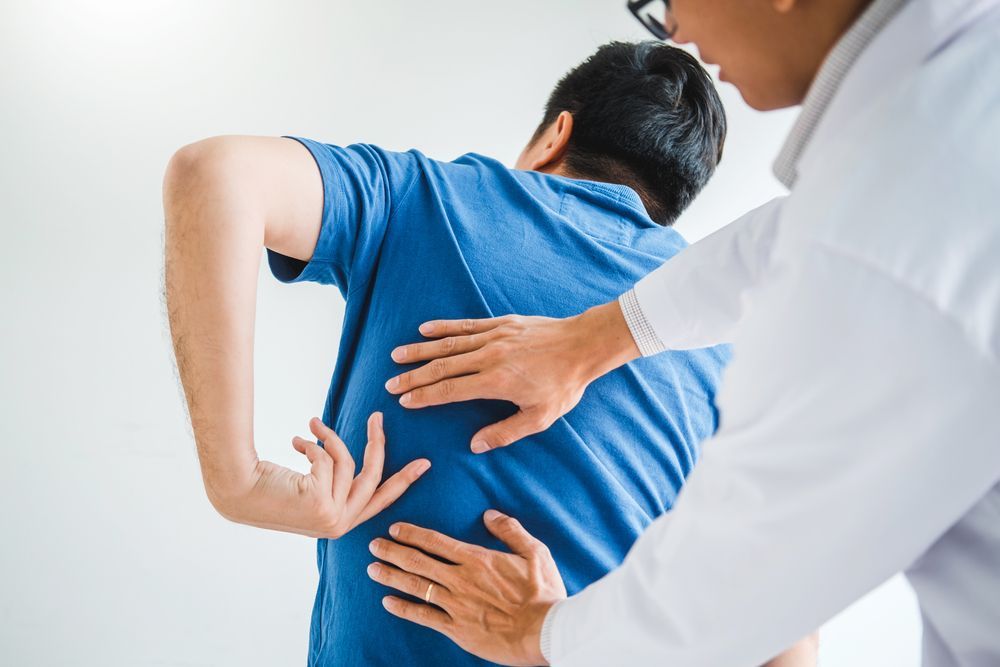 Physical therapist helping a man with back pain stretch in a bright clinic
