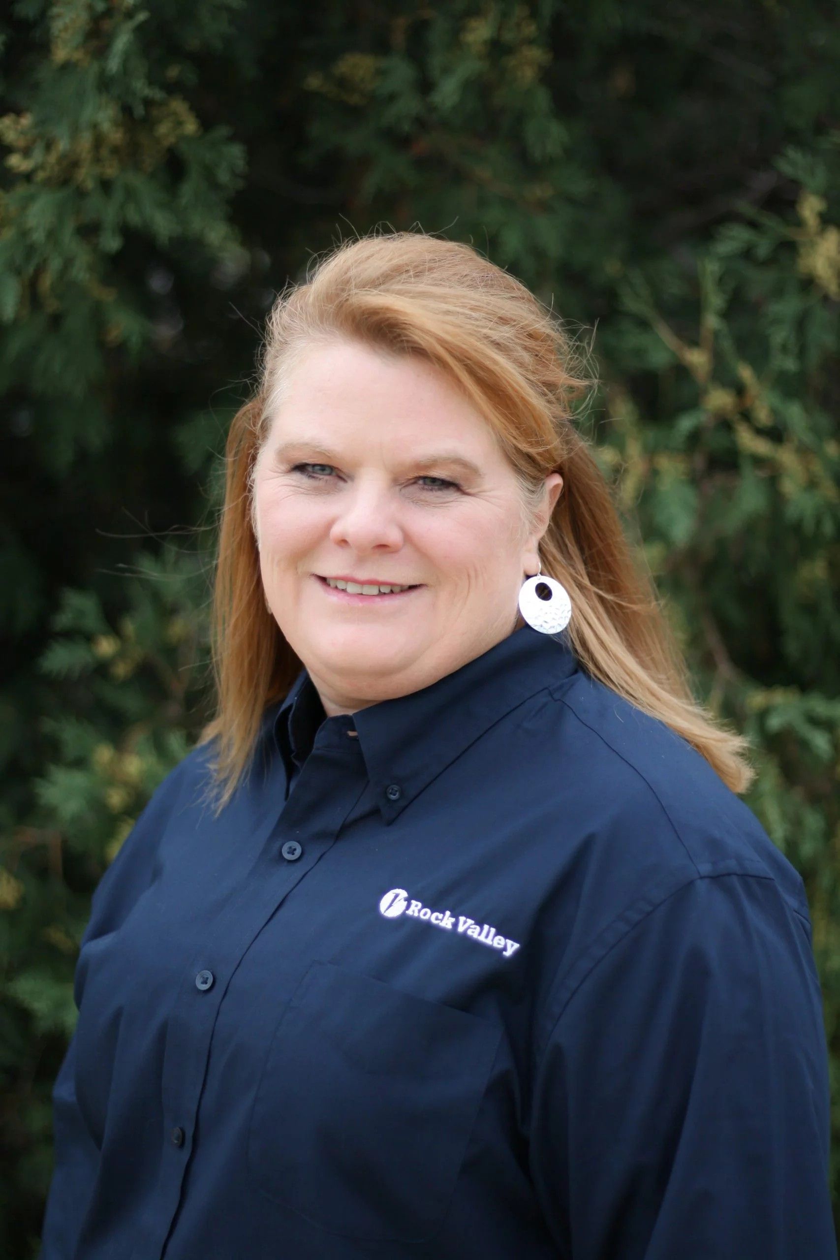 Woman with red hair in blue shirt smiles outside.