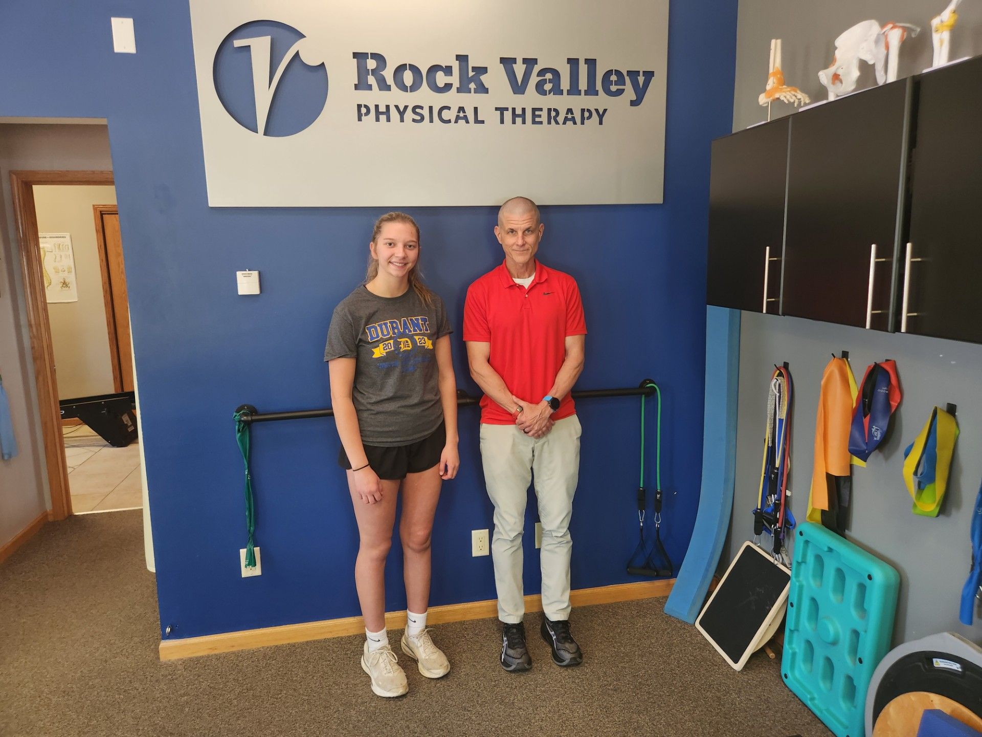 Two people standing in a Rock Valley Physical Therapy lobby, with blue walls and exercise equipment nearby