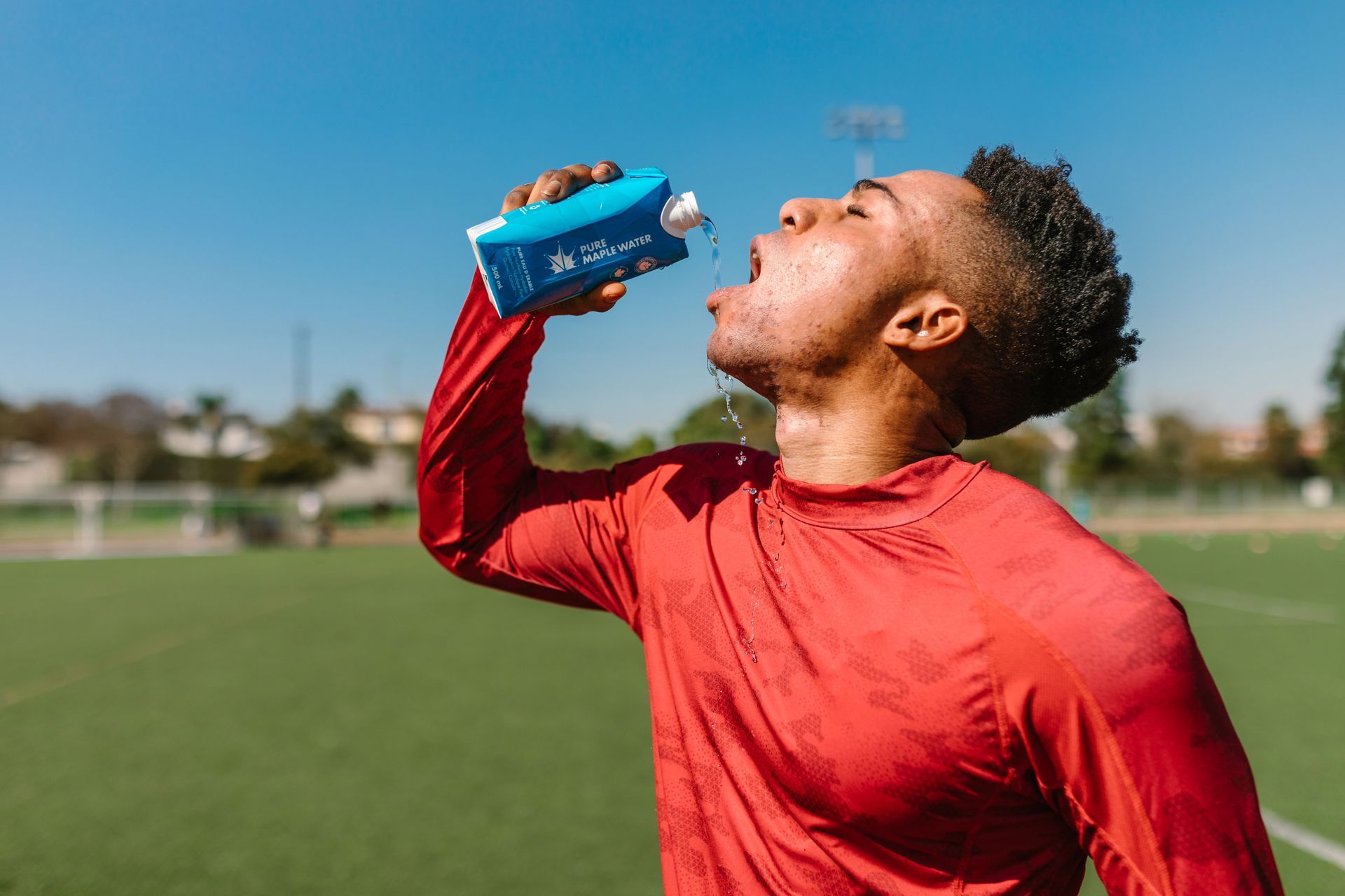 Athlete in red drinking from a blue bottle on a sunny sports field
