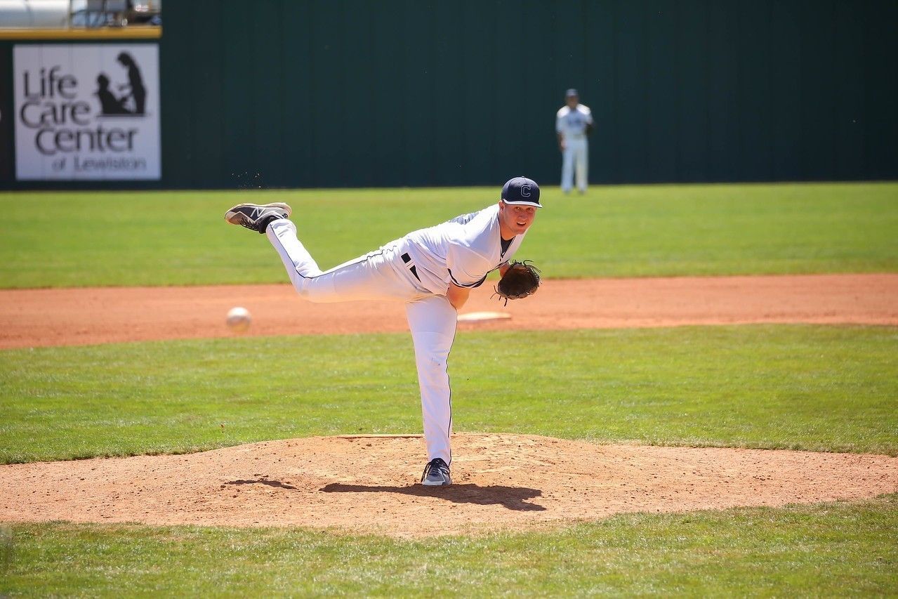 Baseball pitcher in white uniform throwing a pitch on a sunlit mound