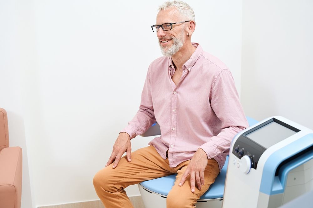 Smiling man seated on a blue exam chair in a medical clinic waiting room