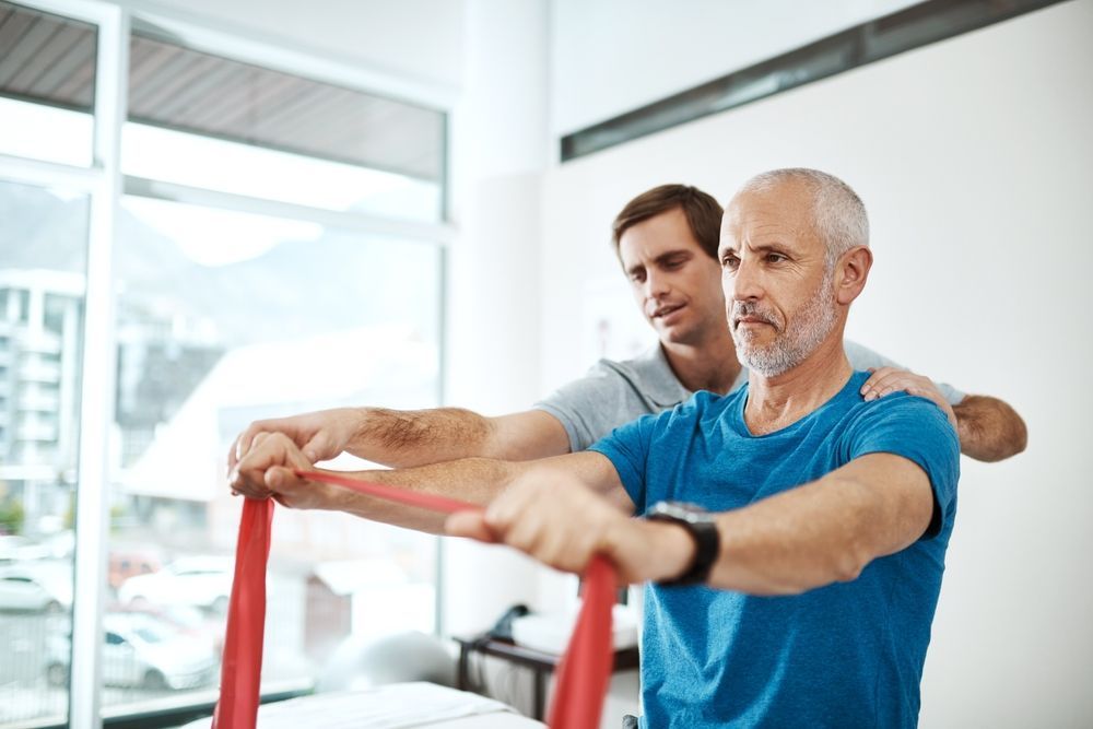 Man in blue shirt doing rehab exercise with therapist in bright gym