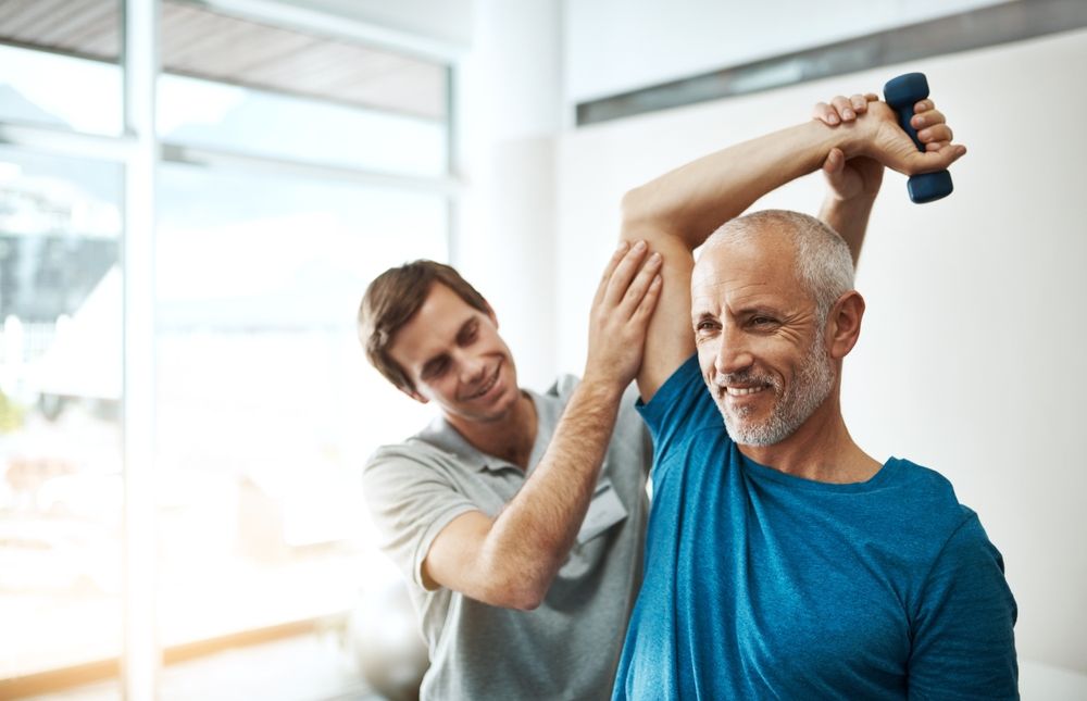 Trainer assisting a client stretching with dumbbells in a bright fitness studio