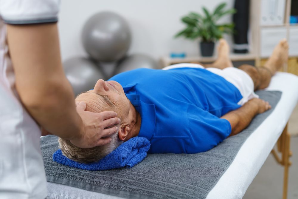 Physical therapist gently stretching a patient’s neck on a treatment table in a bright clinic