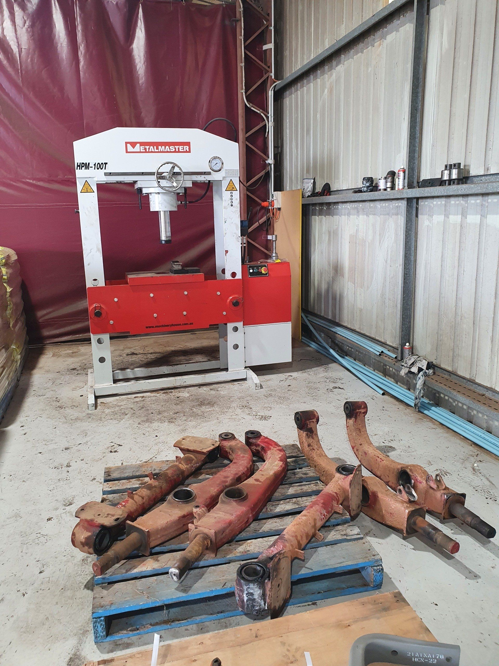 A hydraulic press and metal parts on a pallet in a workshop. The press is red and white.