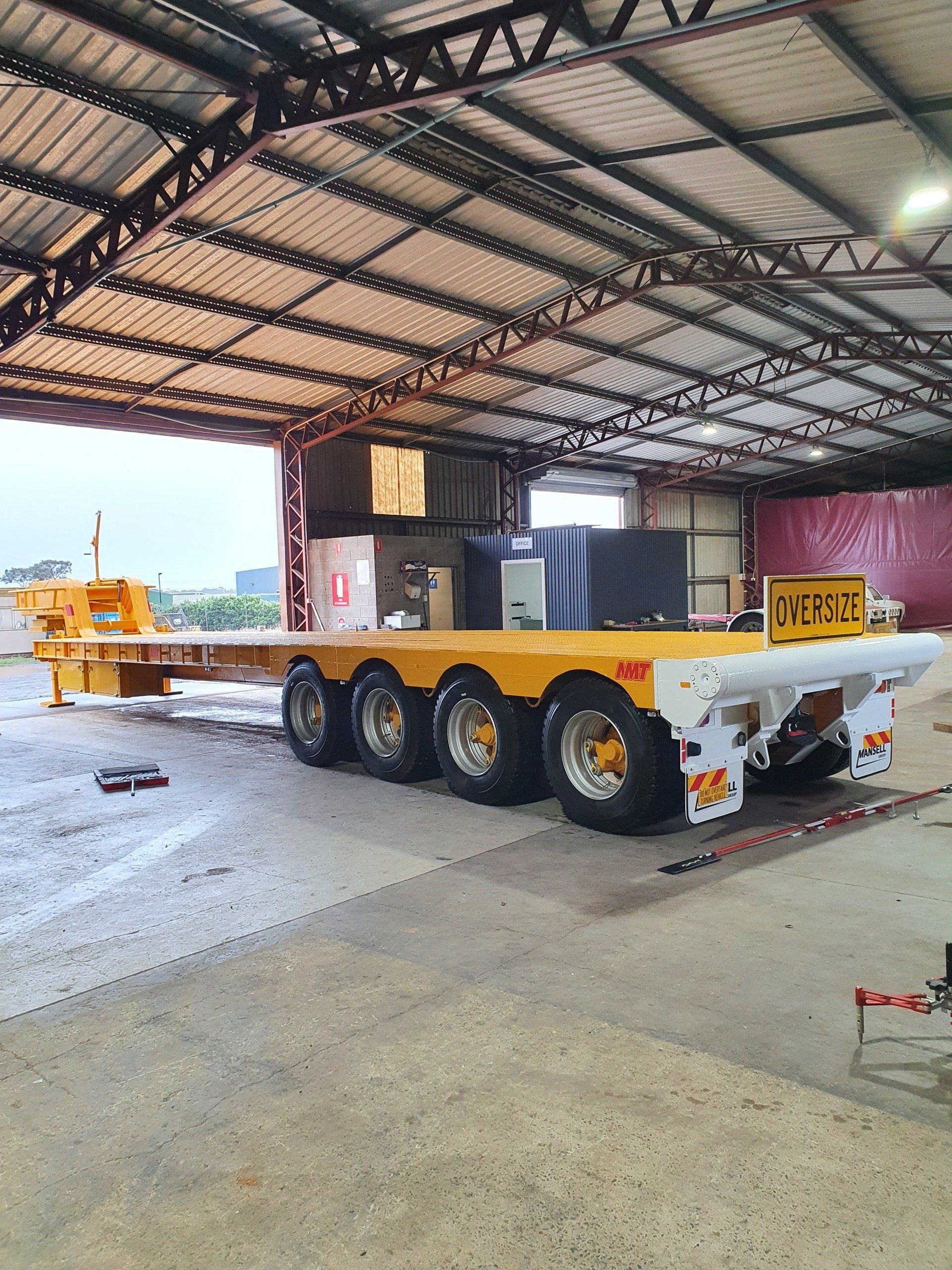 Yellow flatbed trailer parked inside a warehouse with a metal roof.