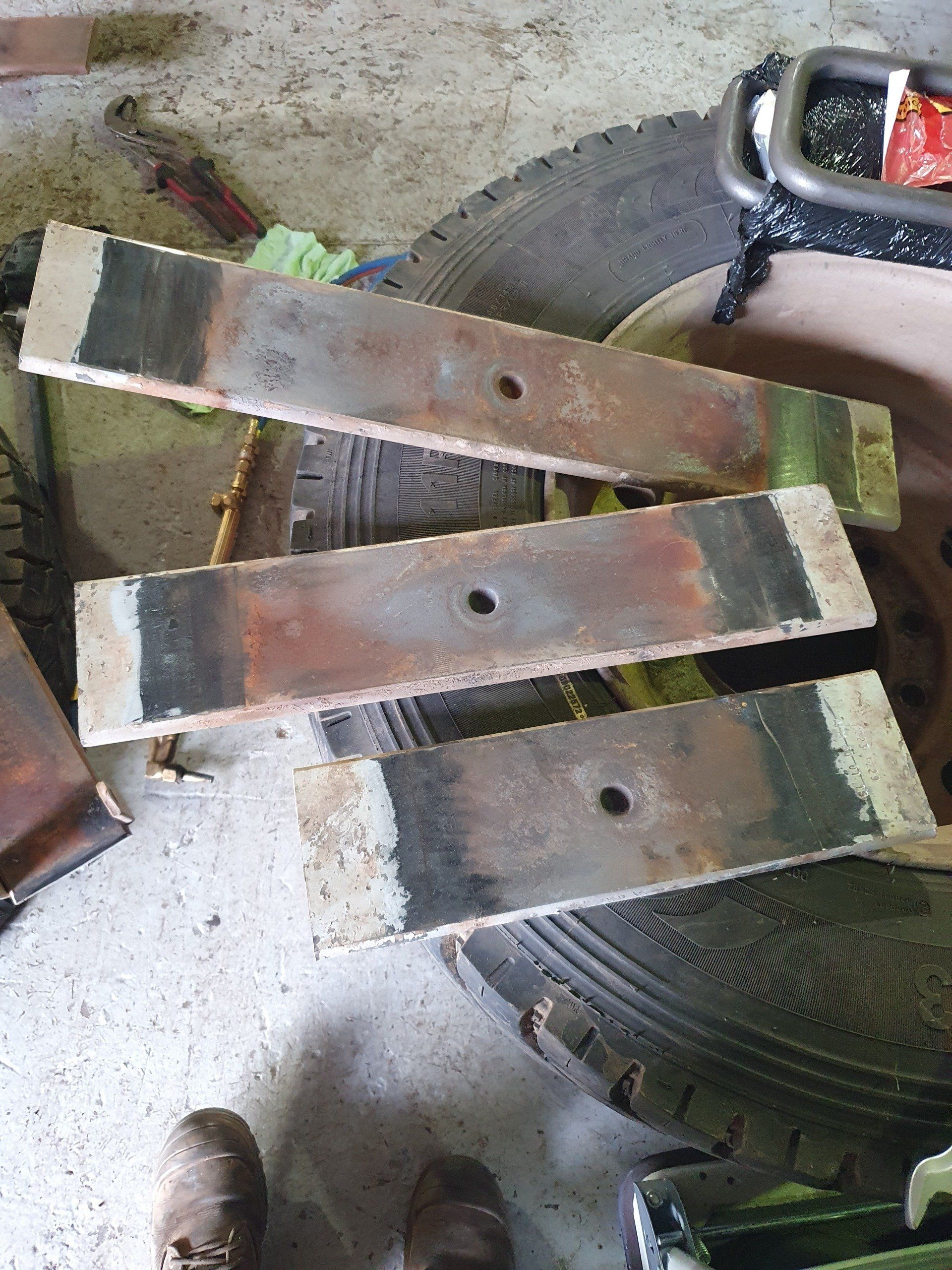 Three rectangular metal plates, rusty with center holes, resting on tires.