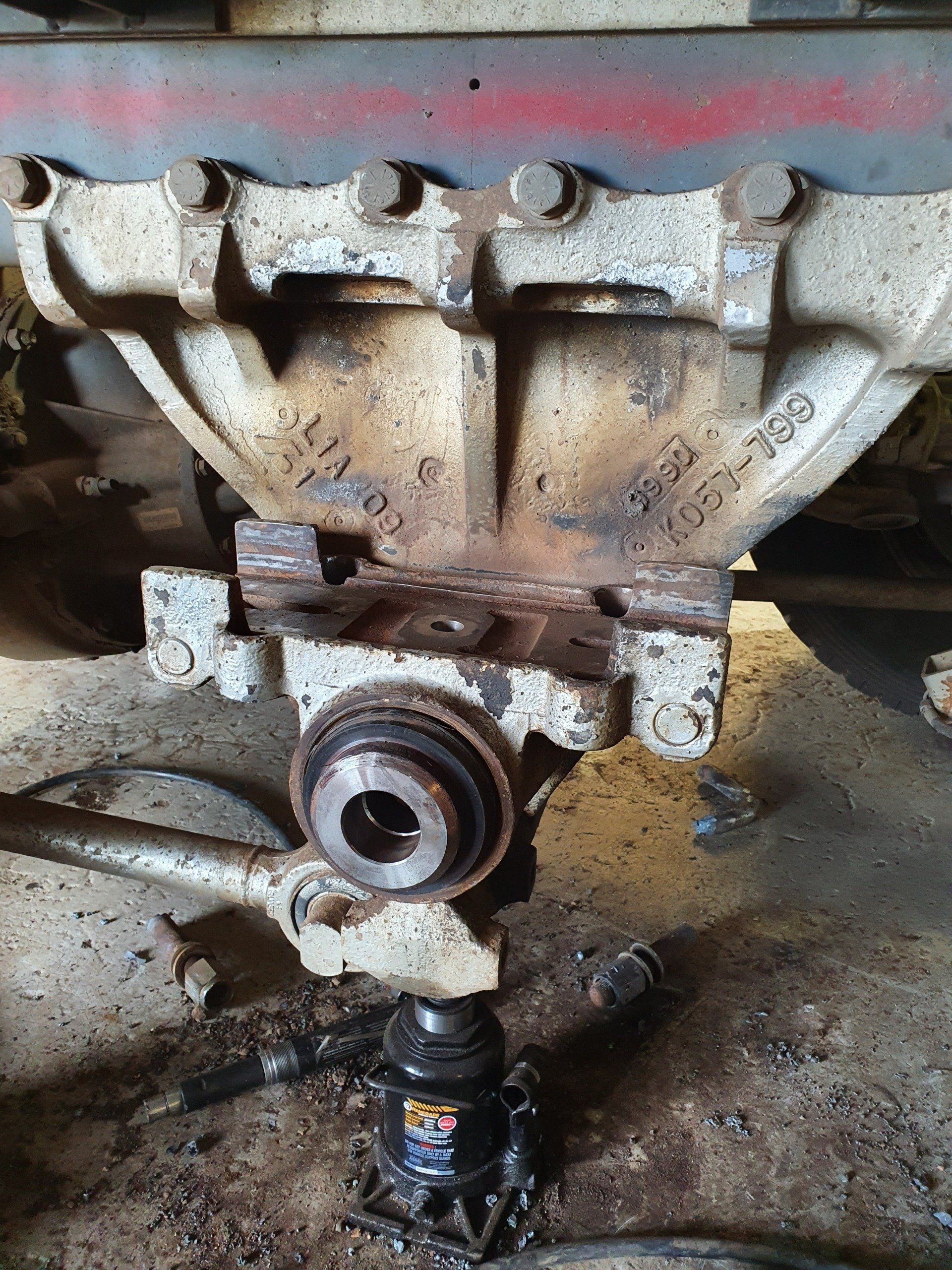 Heavy machinery axle being repaired, jack underneath, showing metal casing and bolts.