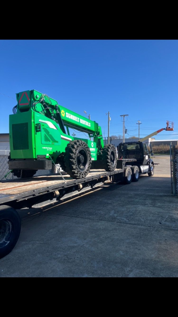 A green crane is sitting on top of a flatbed trailer.