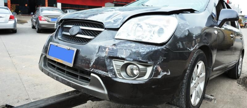Black compact car with front-end damage parked on a street after a collision