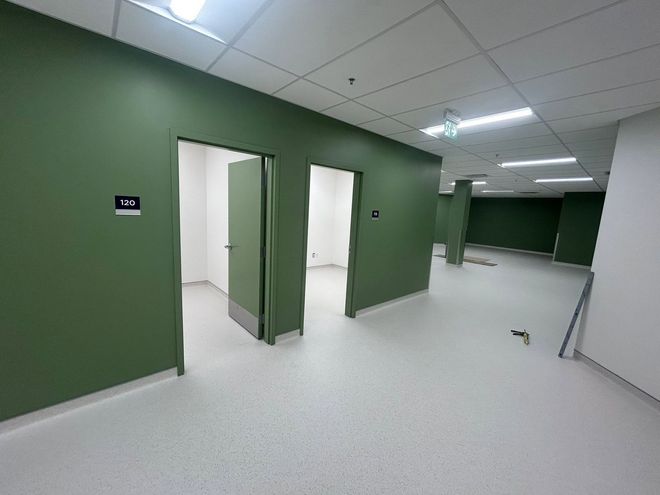 Couloir vert vide avec portes ouvertes, sols blancs et éclairage au plafond dans un bâtiment moderne