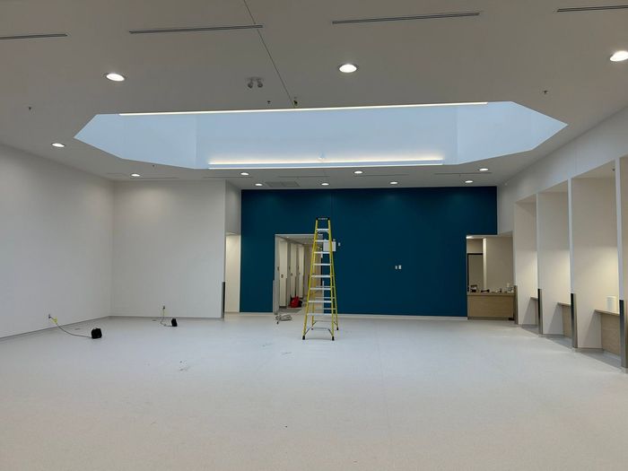 Bureau vide en travaux avec échelle, mur d'accent bleu et éclairage de plafond inachevé