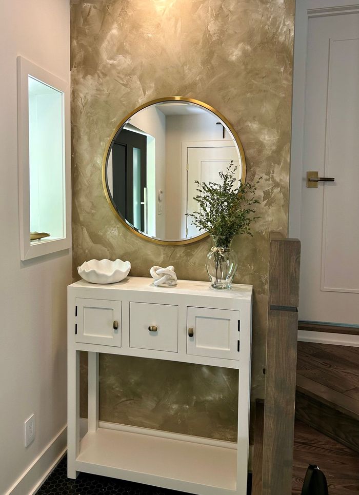 Console blanche avec miroir et objets décoratifs dans un couloir, devant un mur d'accent texturé doré.