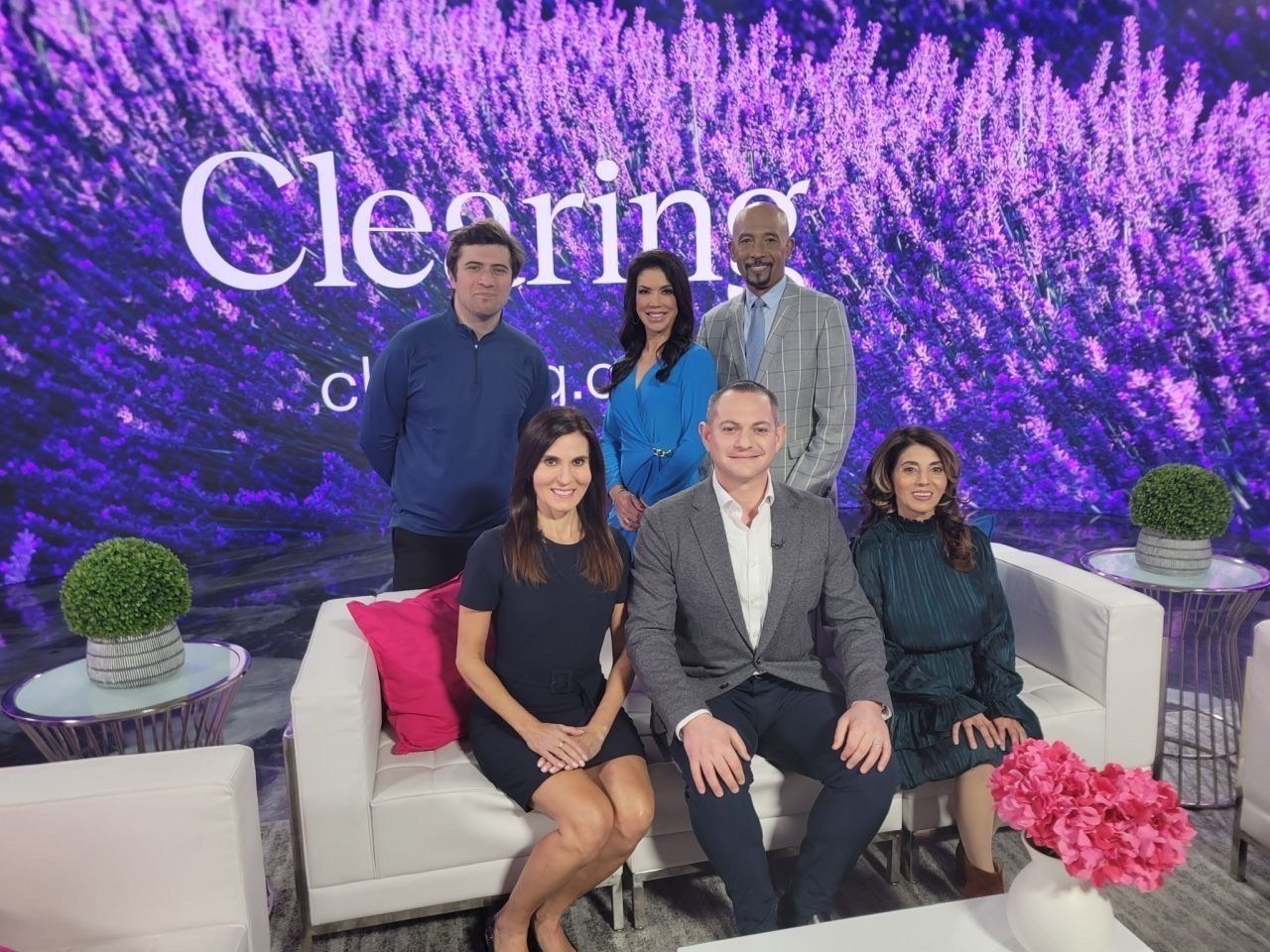 Five people posing on a white couch at a ceremony with purple floral backdrop and pink flowers