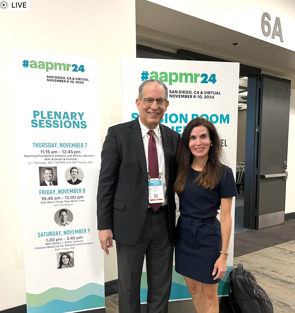 Two people posing at the AAPM 2024 plenary sessions event banner.