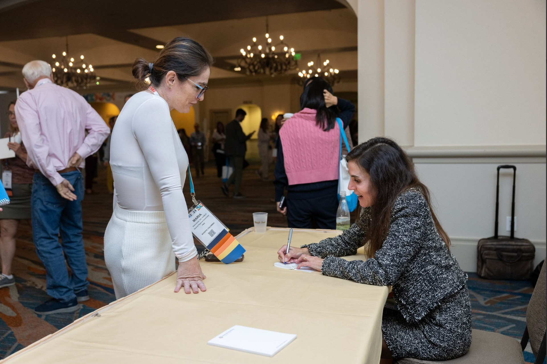 Two women signing papers at a registration table in a hotel lobby