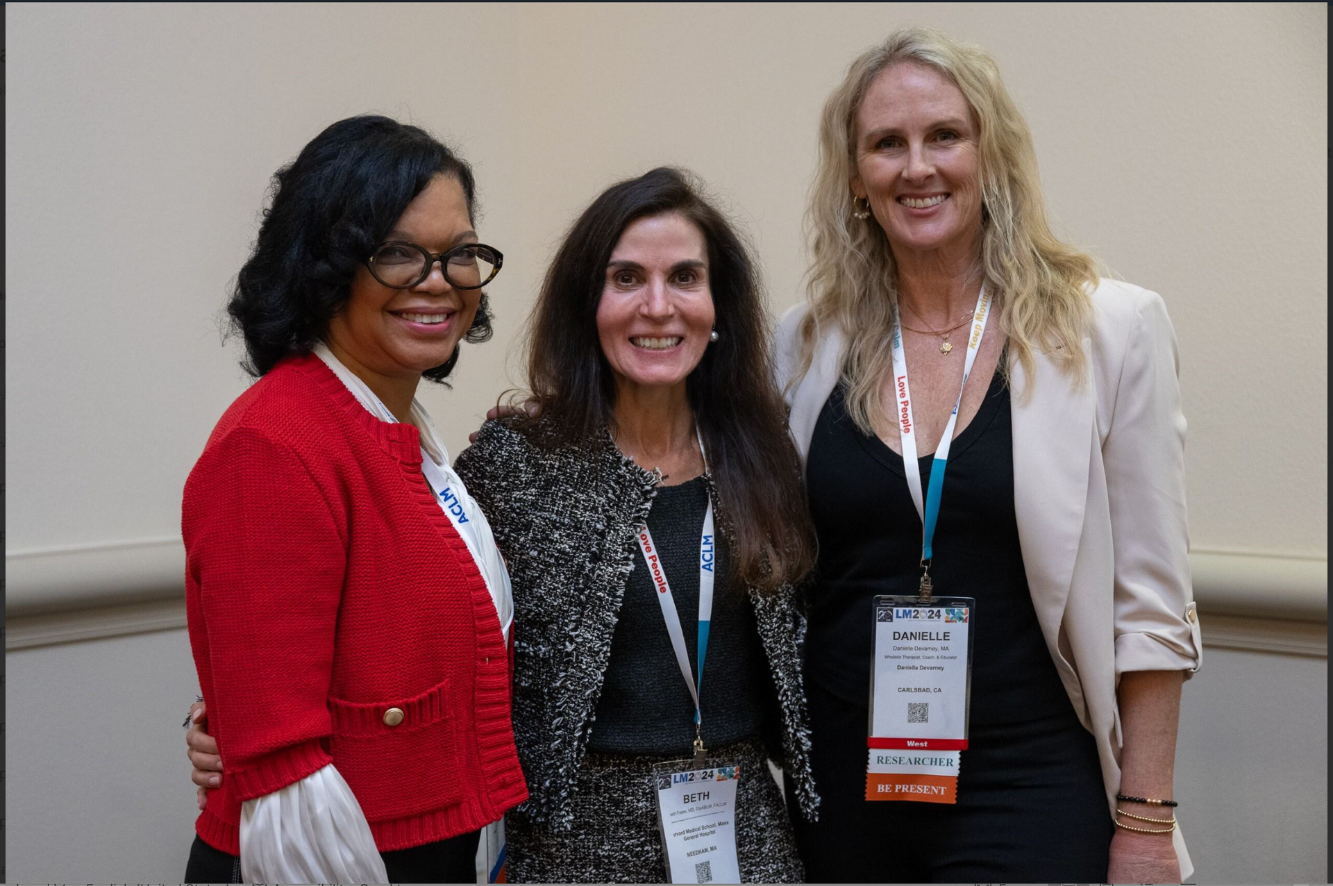 Three women standing together indoors at an event, smiling and wearing lanyards.
