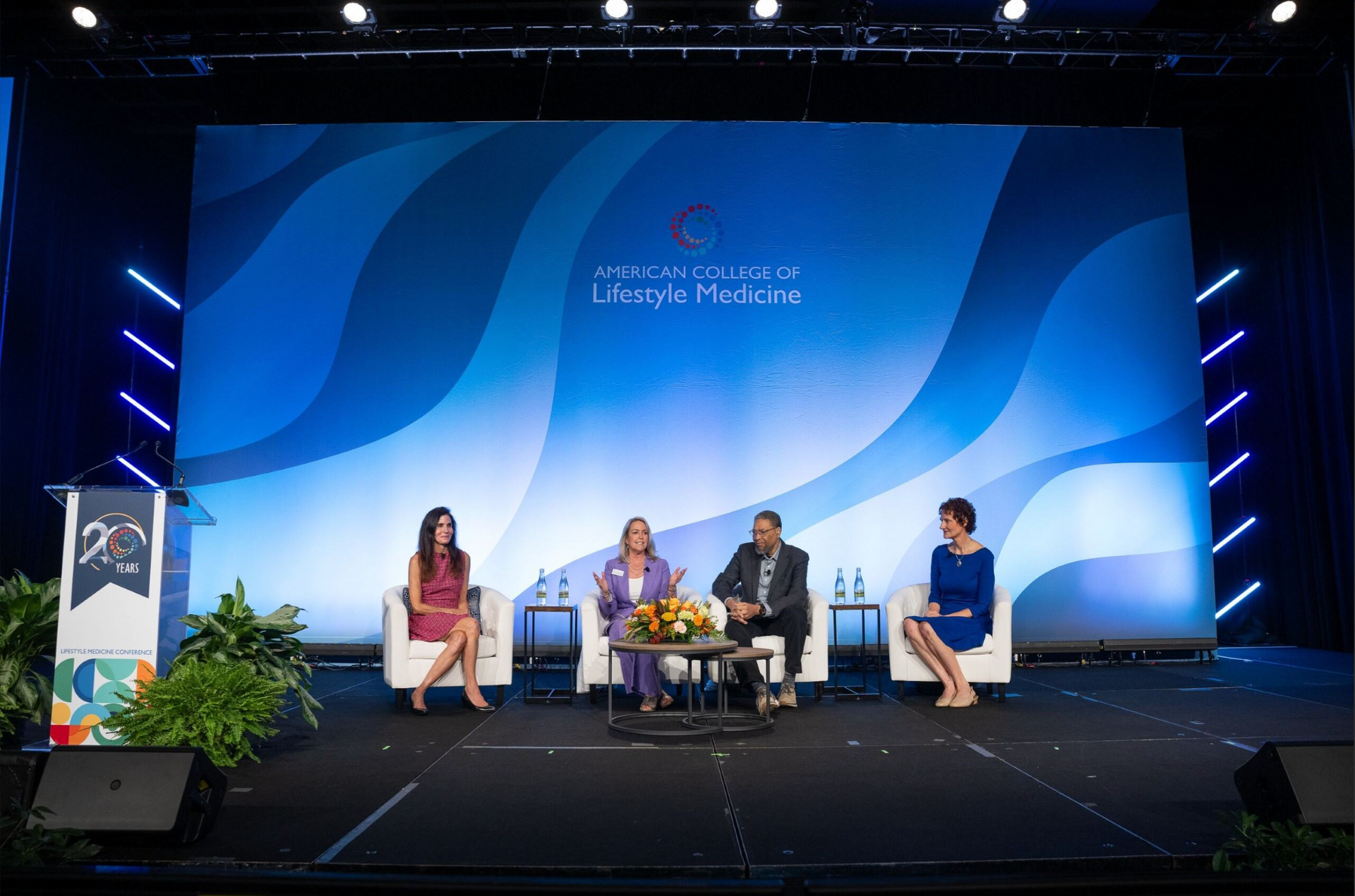 Panel discussion on a blue-lit stage with four seated speakers and a podium at left