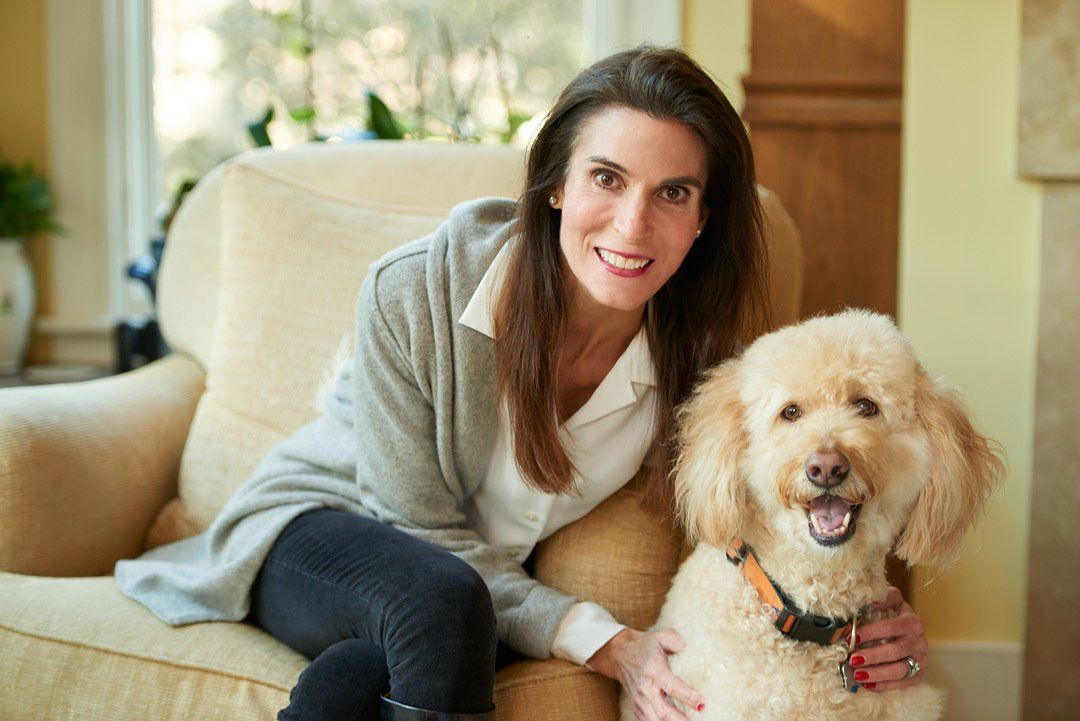Woman sitting on a couch with a fluffy dog indoors, both looking at the camera and smiling