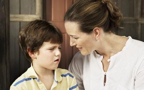 Woman leans toward a concerned boy indoors, speaking closely with him.